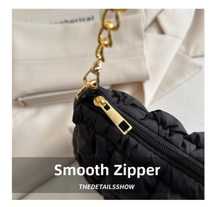 Close-up of a smooth gold zipper on a black quilted cloud bag with metallic chain detail