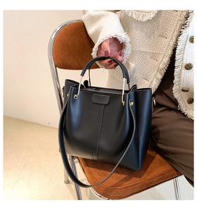 Detail of black PU leather tote bag with gold metal rings and vertical stitching accents
