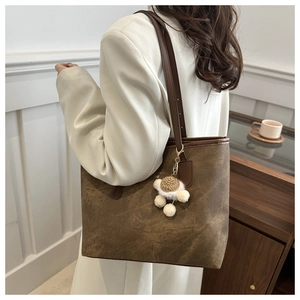 Brown faux leather tote bag with plush ball charm shown over a white blazer