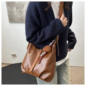 Sac seau en cuir PU marron avec breloque d'ours porté par un mannequin en décor moderne