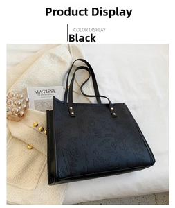 Detail of black tote bag with embossed graffiti pattern and gold rivet accents