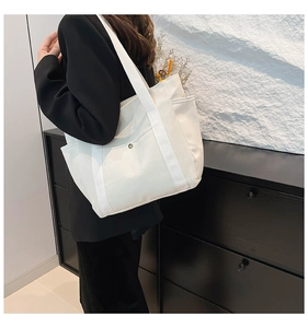 Close-up of minimalist white canvas tote bag with front snap pocket and woven shoulder strap