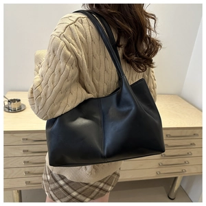 Large black minimalist tote bag worn by a model in a cozy home office setting