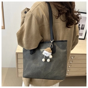 Detail of grey textured tote bag featuring a plush monster charm and long black straps