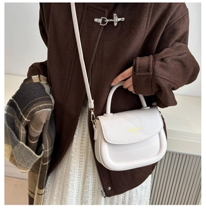 Model wearing a cream semi-circle leather handbag with a top handle and gold lettering
