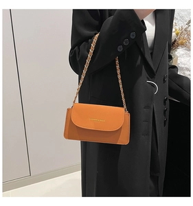Sac à rabat en cuir orange avec chaîne dorée sur fond de blazer noir élégant