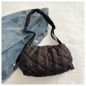 Macro shot of black quilted padded shoulder bag with glossy texture on white fabric