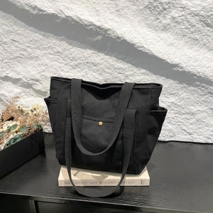 Minimalist large black canvas tote bag with side pockets and golden snap button for commute