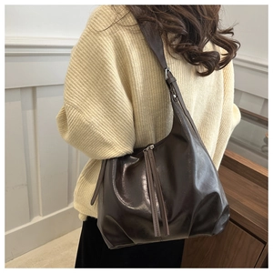 Détail d'un sac cabas marron foncé brillant avec de longs zips à franges sur l'épaule