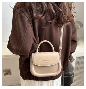 Detail of light apricot saddle bag with gold logo on brown coat background