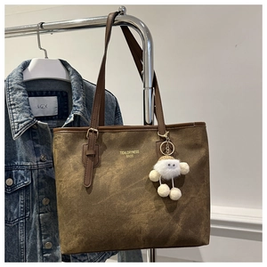 Close-up of brown suede tote bag featuring a plush doll charm and chic shoulder straps