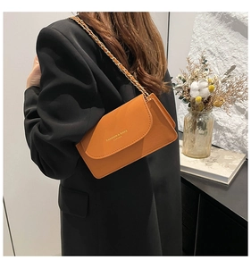 Détail d'un sac bandoulière en cuir marron avec chaîne dorée et logo embossé élégant