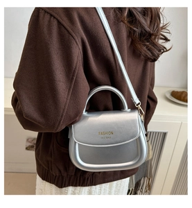 Detail of silver matte saddle bag with rigid top handle and gold foil branding text