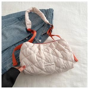 Detail of quilted puffer tote bag with orange strap and fashion bag logo on white fabric