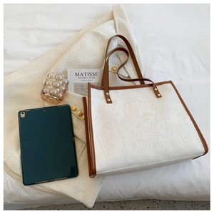 Detail of white tote bag with graffiti embossed patterns and brown rivet handles