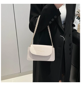 Détail d'un sac à rabat en cuir blanc cassé avec chaîne dorée porté sur un blazer noir