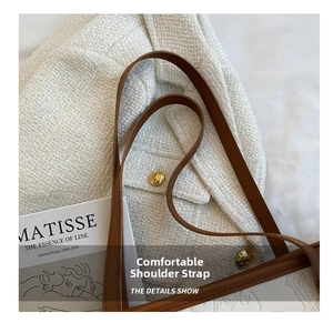 Detail of white embossed leather tote bag with brown shoulder strap on tweed fabric
