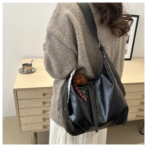 Détail du sac cabas en cuir noir avec bandoulière réglable et breloque ours en peluche