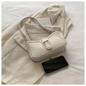 Detail of a creamy white leather shoulder bag with a gold magnetic clasp on soft fabric