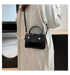 Close-up of black crossbody bag with glossy leather finish and golden metallic buckles