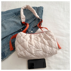 Close-up of beige quilted tote bag featuring a contrast orange strap and fashion label