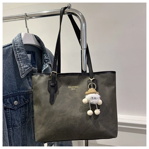 Detail of grey-green suede tote bag with leather strap and white cloud plush charm