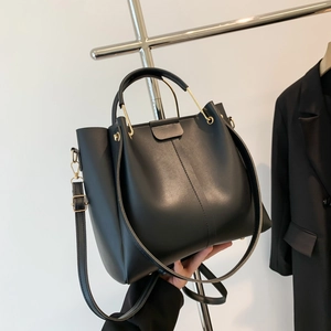 Black PU leather tote bag with gold metal handle and shoulder strap on display stand