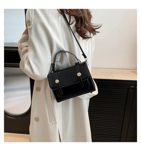 Detail of a black patent leather shoulder bag with gold studs on white trench coat