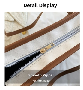 Detailed close-up of smooth gold metal zipper and brown leather trim on a tote bag