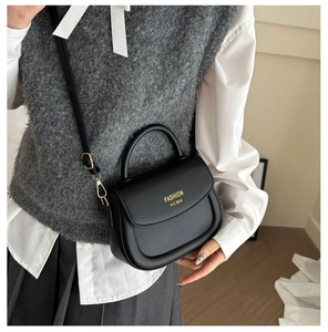 Close-up of black matte leather saddle bag featuring gold fashion lettering and handle