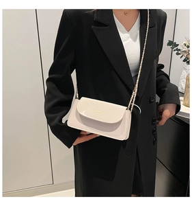 Détail du sac carré en cuir crème avec lettrage doré et chaîne sur un blazer noir