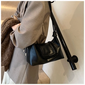 Detail view of black leather shoulder bag with ruffled flap on a grey blazer outfit