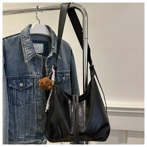 Détail du sac hobo noir brillant avec une breloque d'ours en peluche sur la bandoulière