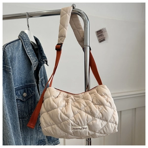 Macro detail of beige quilted puffer tote bag with orange strap accent and textile label