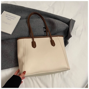 Detail view of a beige tote bag with brown leather handles on a grey coat with a prop book