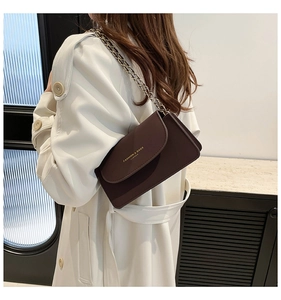 Détail d'un sac à rabat en cuir marron avec lettrage doré et bandoulière chaîne sur modèle