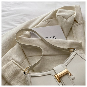 Creamy white leather underarm bag with gold buckle on a stylish tweed jacket
