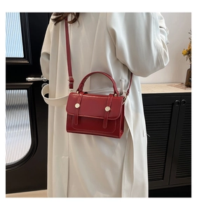 Detail of red glossy small square bag with golden buttons worn on a white coat