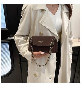 Détail du sac bandoulière en cuir marron foncé avec chaîne dorée et inscription imprimée