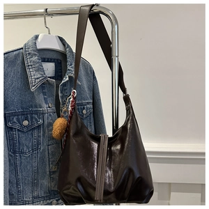 Détail du sac hobo en cuir marron foncé brillant avec large bandoulière et pompon