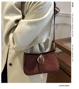 Detail of dark brown suede vintage shoulder bag with golden buckle on a beige coat