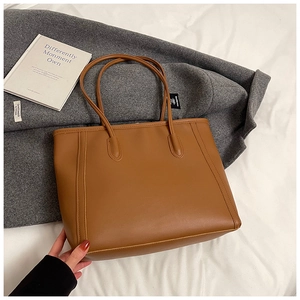 Detail of caramel leather tote bag with vertical stitching on white fabric surface