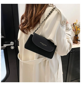 Détail du sac bandoulière en cuir noir avec chaîne dorée sur un mannequin en trench