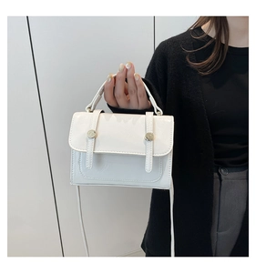 Detail of off-white faux leather crossbody bag with golden metal buckle and top handle