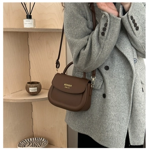 Detail view of a dark brown leather saddle bag styled on a herringbone blazer