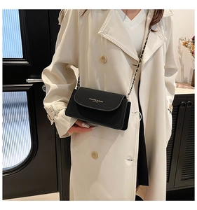 Détail d'un sac à rabat en cuir noir avec lettrage doré et bandoulière chaîne sur mannequin