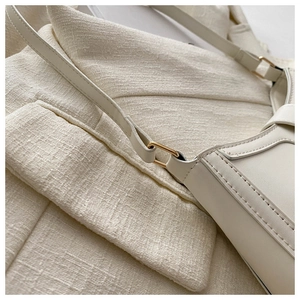Detail of minimalist cream handbag showing gold metal buckles and neat stitching