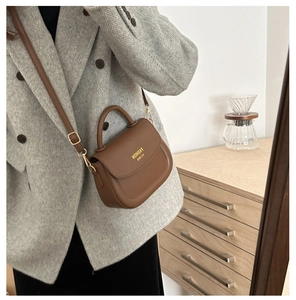 Detailed side view of a brown leather saddle bag with adjustable strap and gold logo