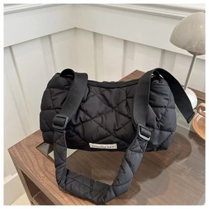 Detailed view of black quilted nylon bag with a minimalist white logo patch on a wooden table
