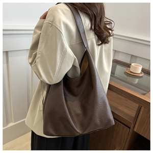 Detail of a large brown leather tote bag with wide strap in a cozy cafe setting